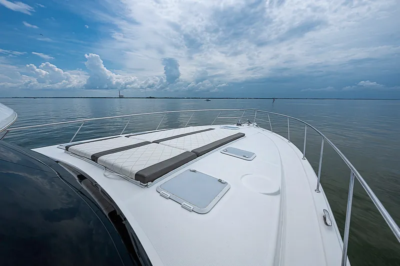Slide: The Image of 2009 Riviera 58 Flybridge yacht deck with sun loungers, calm sea, and cloudy sky. - 89