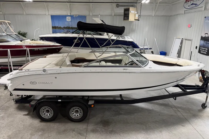 Slide: The Image of 2013 Cobalt 220 boat on trailer in showroom, featuring sleek white design and black canopy. - 13