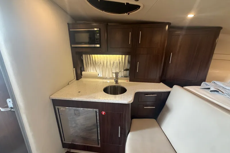 Slide: The Image of 2017 Regal 32 Express yacht interior kitchen with microwave, sink, and dark wood cabinetry. - 13