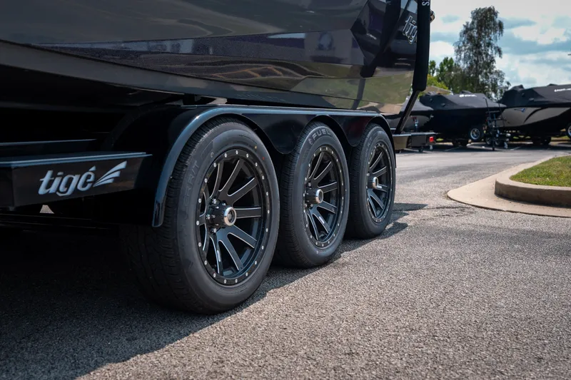 Slide: The Image of 2026 Tigé Ultré 25ZX boat trailer with sleek black wheels on a sunny day. - 2