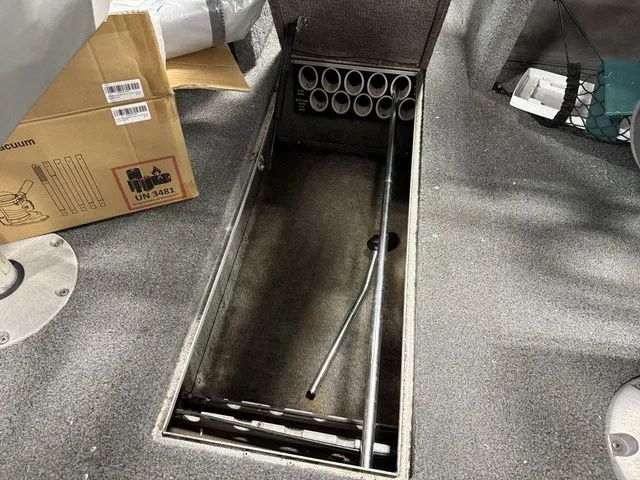 Slide: The Image of An open storage compartment on a 2006 Lund 1800 Fisherman boat, featuring rod holders and a gray floor. - 21