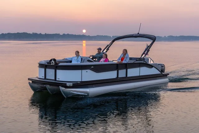 The Image of A sleek pontoon boat cruises on a calm lake at sunset. Four people are seated comfortably on board. - 1