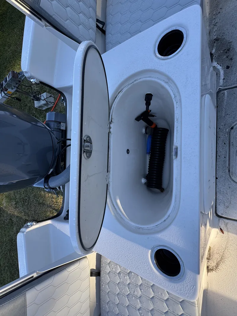 Slide: The Image of An open storage compartment on a Carolina Skiff 23 LS boat, with a hose and engine in the background. - 6