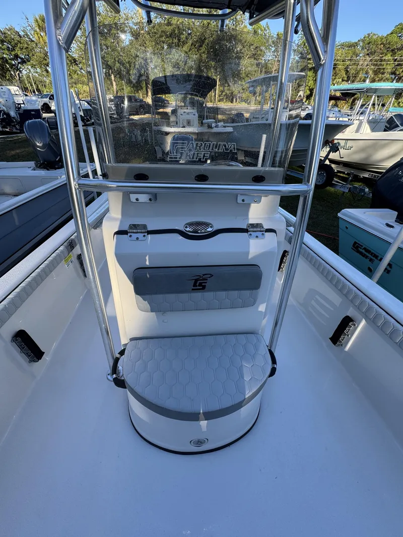 Slide: The Image of The image shows the cockpit of a Carolina Skiff 23 LS boat. It features a white console with a padded seat and steering wheel. Other boats and trees are visible in the background. - 17