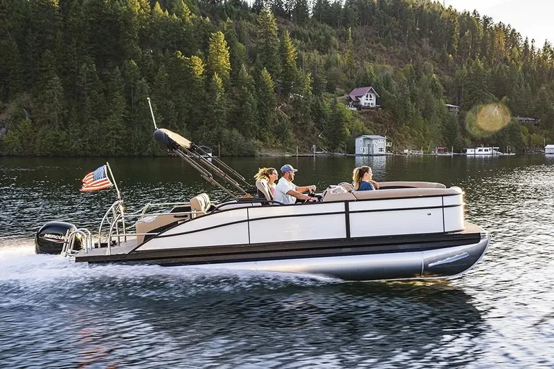 The Image of A 2027 Barletta C24U pontoon boat cruises on a calm lake, surrounded by wooded hills. - 1