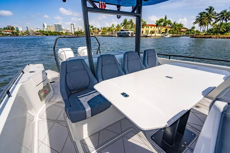 Slide: The Image of 2021 Axopar Brabus 37 Sun-Top boat interior with seating and table, scenic waterfront view. - 18