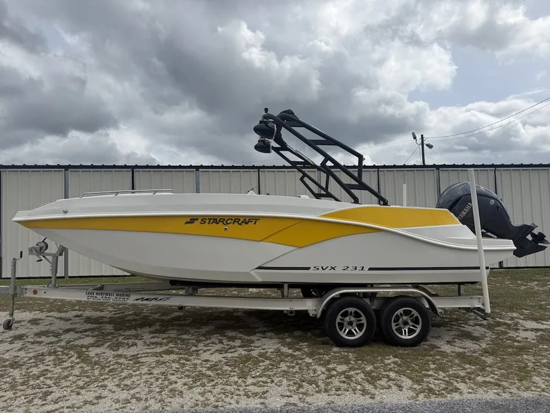 Slide: The Image of A yellow and white Starcraft SVX 231 OB boat from 2025 on a trailer in front of a building. - 2