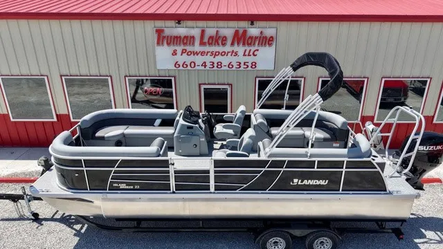 Slide: The Image of A Landau Island Breeze 23C Sport Rear Lounge Tritoon on a trailer in front of a building. - 10