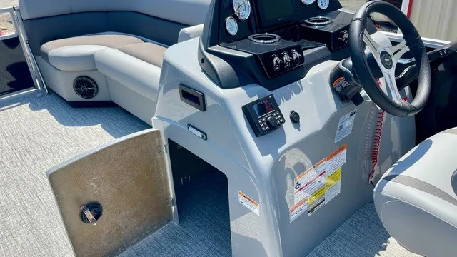 Slide: The Image of The image shows the cockpit of a Landau Island Breeze 23C Sport Rear Lounge Trit pontoon boat. It features a modern dashboard with multiple gauges and a steering wheel. Padded seating is visible in the background. - 18