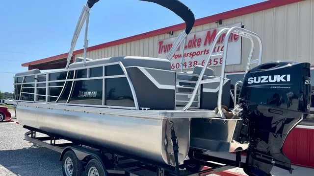Slide: The Image of A modern pontoon boat with a Suzuki outboard motor, parked on a trailer in front of a building. - 5