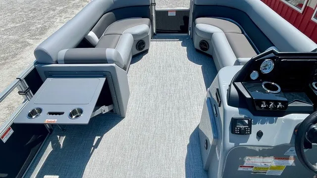 Slide: The Image of The image shows the interior of a Landau Island Breeze 23C Sport Rear Lounge Trit pontoon boat. It features gray upholstery and a modern dashboard. - 7
