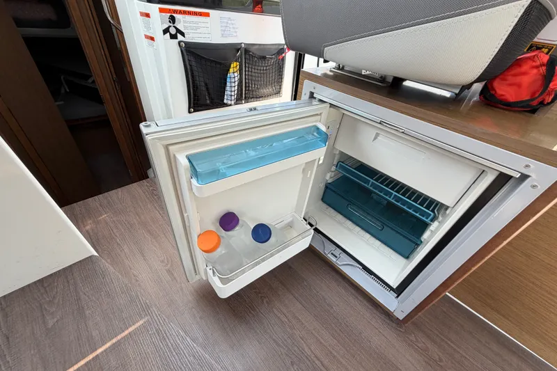 Slide: The Image of Open fridge inside 2020 Jeanneau NC Sport 895 boat, showing interior storage and bottles. - 62