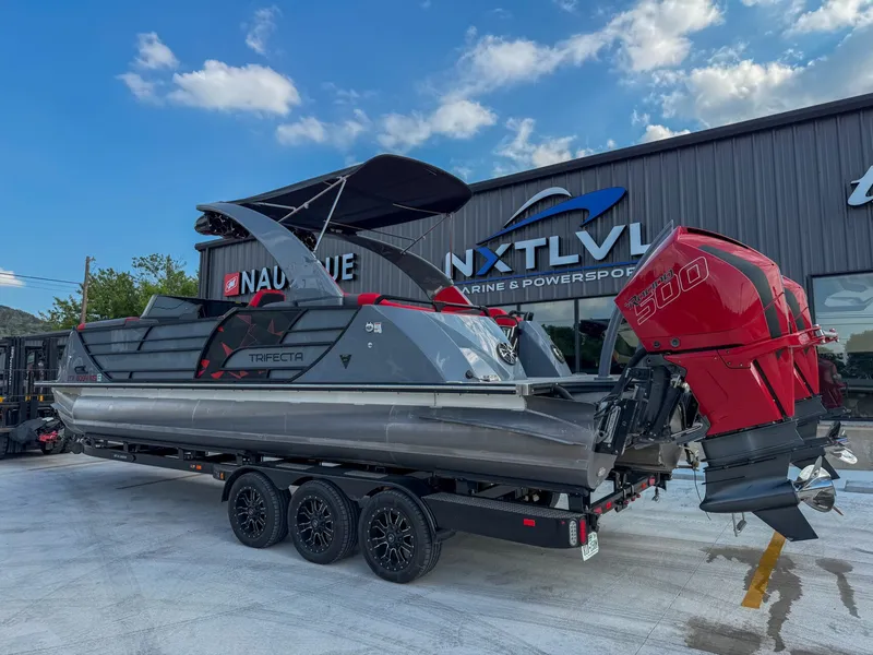 Slide: The Image of A modern Trifecta pontoon boat with a red outboard motor sits on a trailer in front of a building. - 3