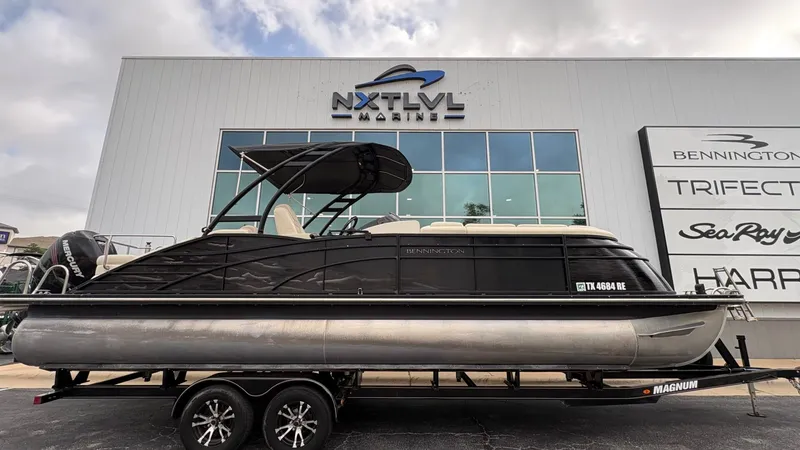 The Image of A 2015 Bennington 2575 QCW pontoon boat on a trailer in front of a modern building. - 1