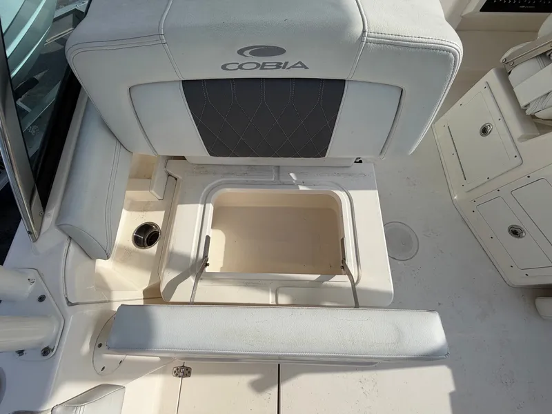 Slide: The Image of The 2021 Cobia 240 Dual Console features an open storage compartment beneath a cushioned seat. - 25