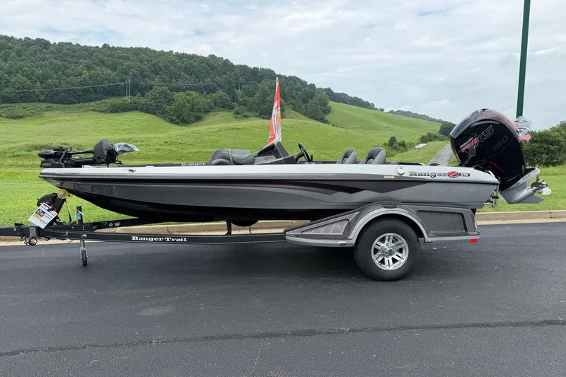 Slide: The Image of 2025 Ranger Z518 Cup-Equipped boat on trailer, parked on asphalt with green hills background. - 1