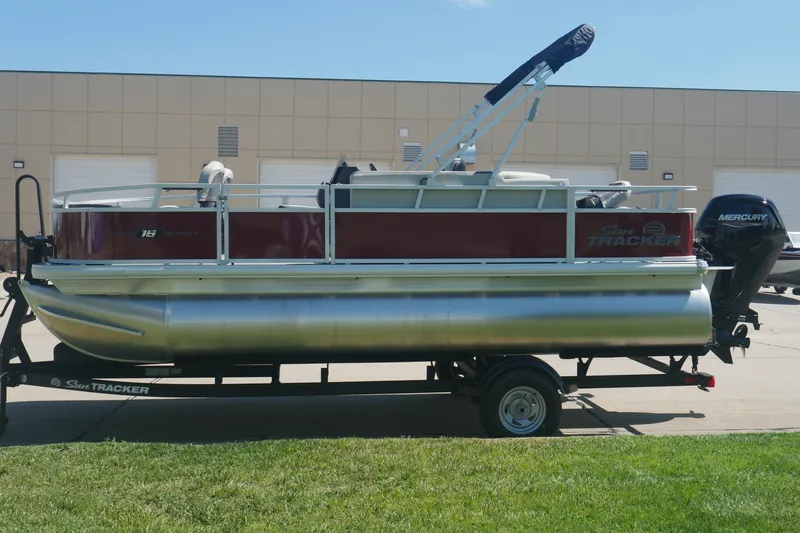 Slide: The Image of 2026 Sun Tracker Bass Buggy 18 DLX pontoon boat on trailer, parked outdoors. - 2