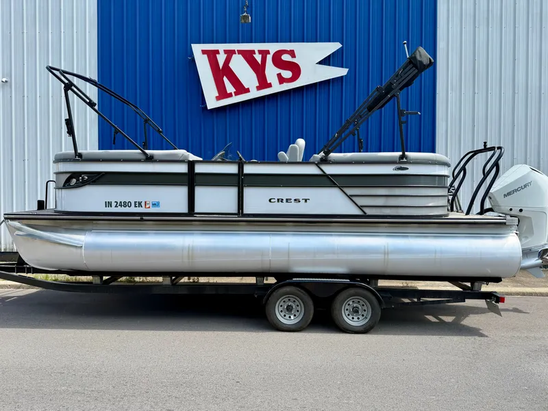 The Image of A 2022 Crest Classic Platinum 220 SLC pontoon boat on a trailer in front of a blue building. - 0