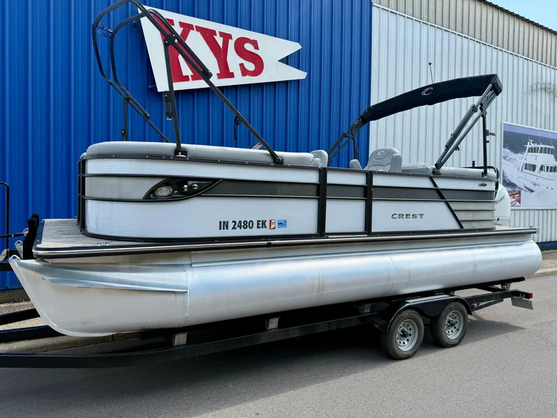 Slide: The Image of A 2022 Crest Classic Platinum 220 SLC pontoon boat on a trailer in front of a blue building. - 4