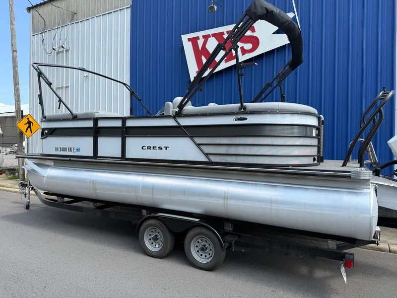 Slide: The Image of A 2022 Crest Classic Platinum 220 SLC pontoon boat on a trailer in front of a blue building. - 17