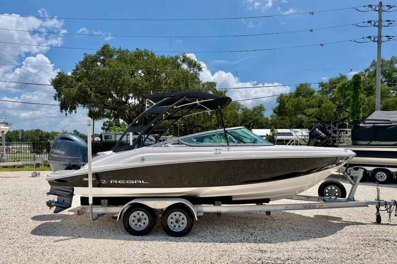 Slide: The Image of 2020 Regal 21 OBX boat on trailer, parked outdoors under a clear blue sky. - 4