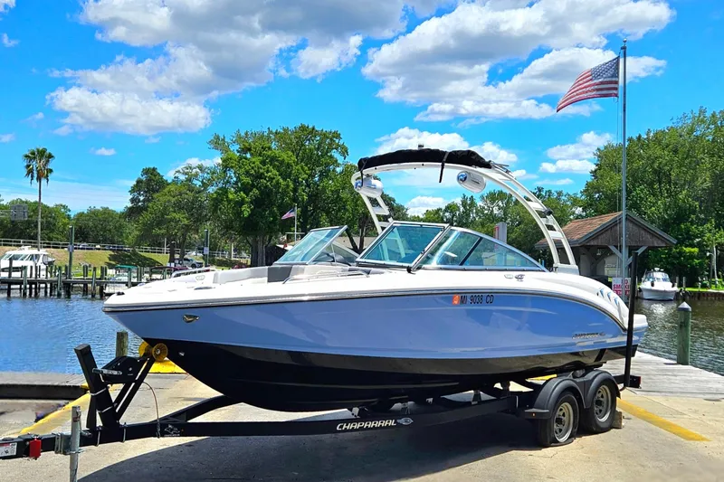 Slide: The Image of 2023 Chaparral 23 SSi boat on trailer by a scenic waterfront with American flag. - 2
