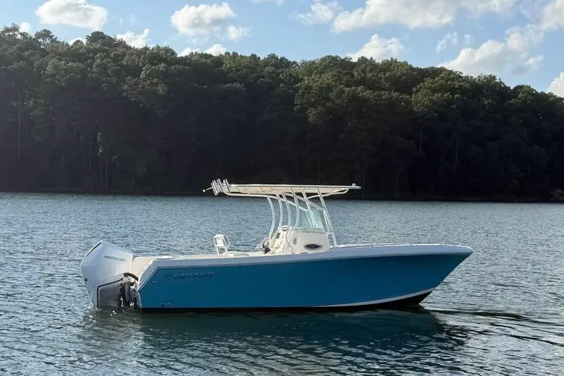 Slide: The Image of 2022 Sailfish 242 CC boat on a serene lake with forested background. - 2