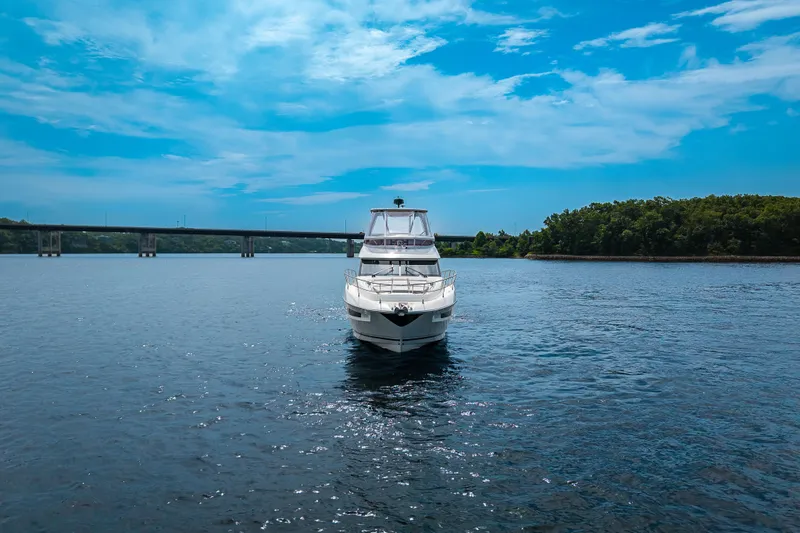 Slide: The Image of 2025 Pacific Prestige 460 Fly yacht on serene water with bridge and trees in background. - 2