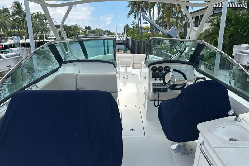 Slide: The Image of 2015 Boston Whaler 270 Vantage boat interior with steering console and seating, docked by palm trees. - 34