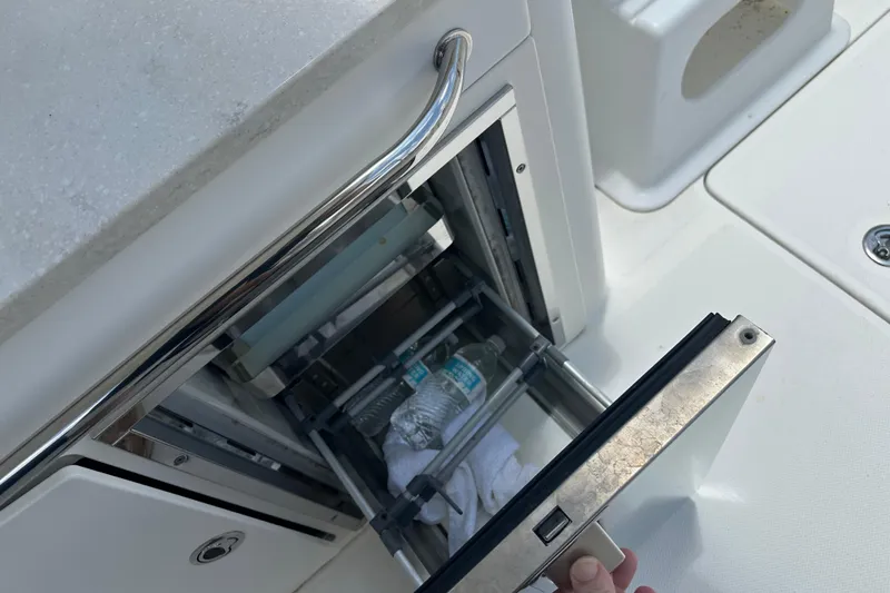 Slide: The Image of Open storage compartment on 2015 Boston Whaler 270 Vantage boat, containing water bottles and a towel. - 32