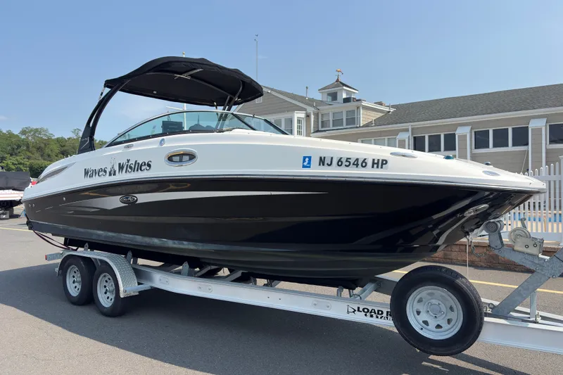 The Image of 2014 Sea Ray 260 Sundeck boat on trailer, labeled "Waves & Wishes," parked near a building. - 0