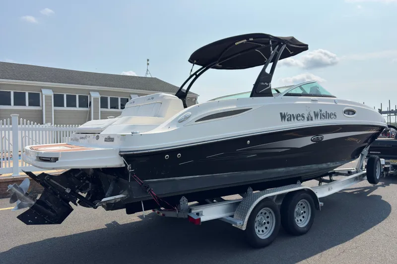 Slide: The Image of 2014 Sea Ray 260 Sundeck boat on trailer, named "Waves & Wishes," parked near a building. - 6