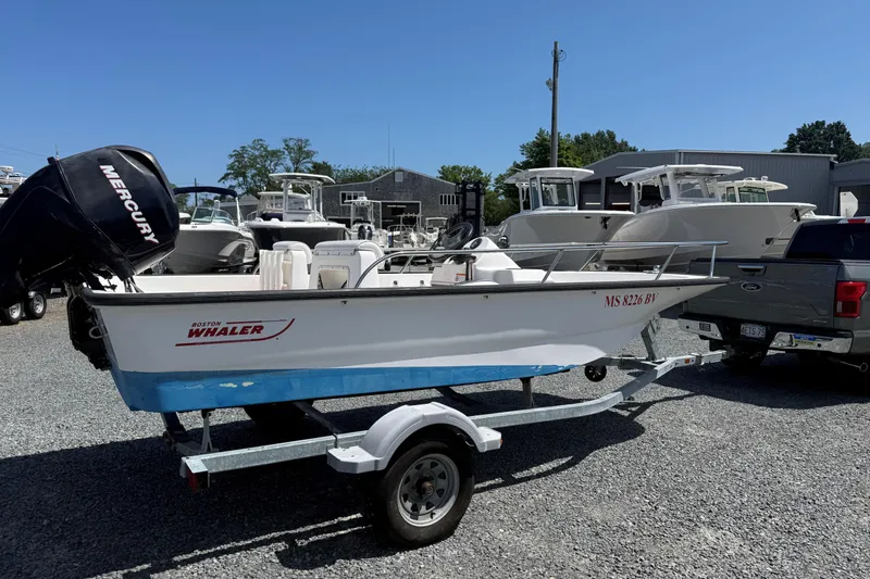 The Image of 2008 Boston Whaler 150 Sport boat on trailer, parked outdoors with other boats. - 0