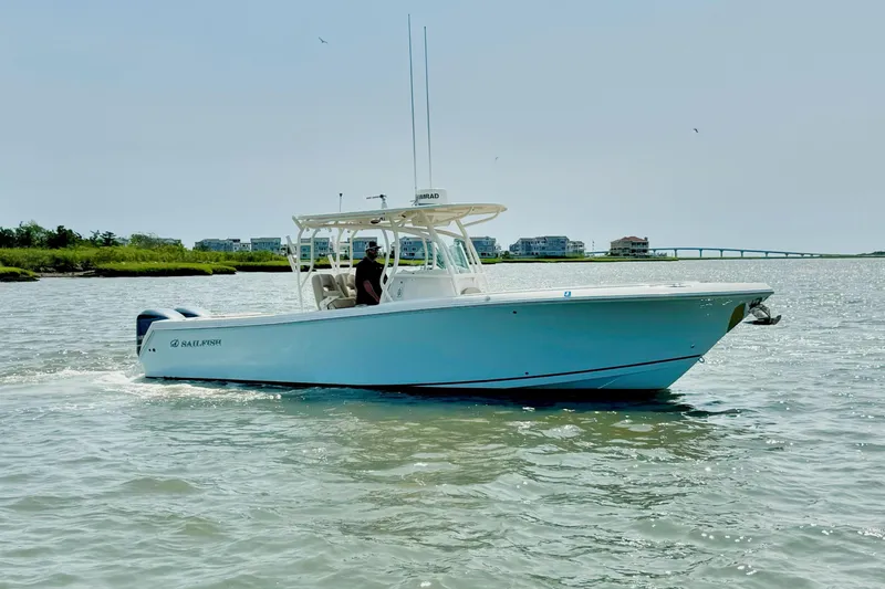 Slide: The Image of 2017 Sailfish 290 CC boat cruising on a sunny day near coastal homes and a bridge. - 9
