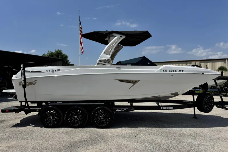 Slide: The Image of 2025 Tigé 24RZX boat on trailer, white exterior, parked outdoors with American flag. - 4