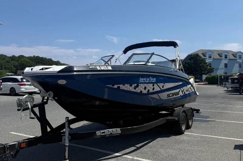 Slide: The Image of 2020 Scarab 255 Open ID boat on trailer in parking lot under clear sky. - 4