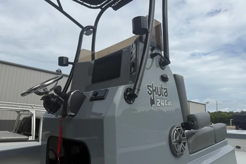 Slide: The Image of 2027 Skuta 24 Cat boat console with steering wheel and controls under cloudy sky. - 7