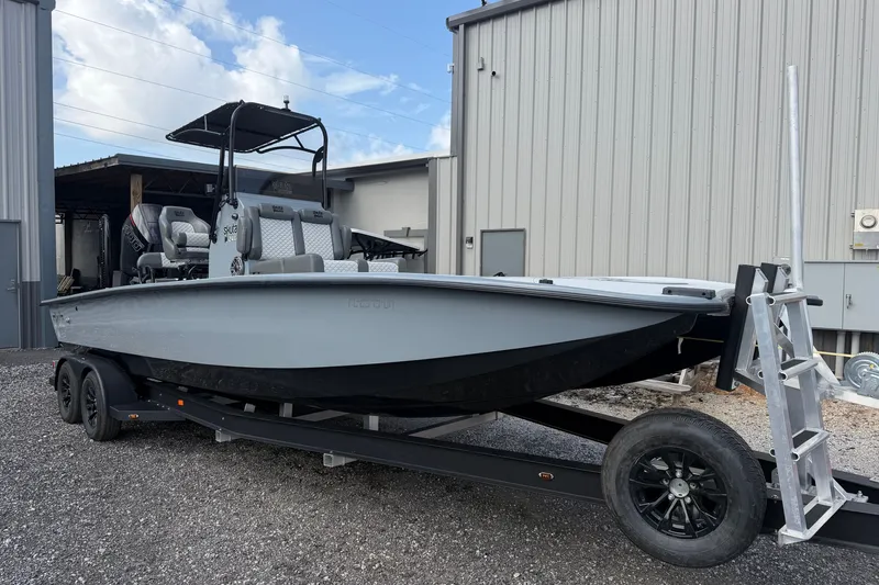 Slide: The Image of 2027 Skuta 24 Cat boat on trailer, parked outside industrial building. - 24