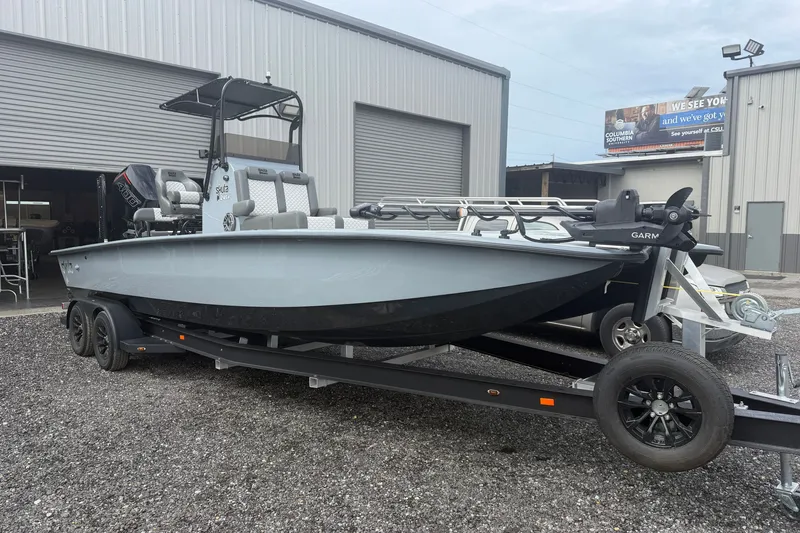 Slide: The Image of 2027 Skuta 24 Cat boat on trailer outside industrial building. - 2