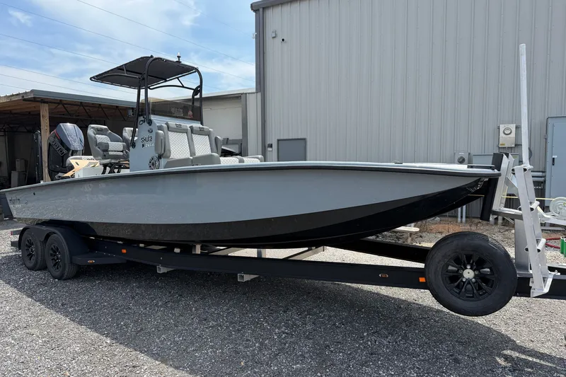 Slide: The Image of 2027 Skuta 24 Cat boat on trailer, parked outside a metal building. - 23