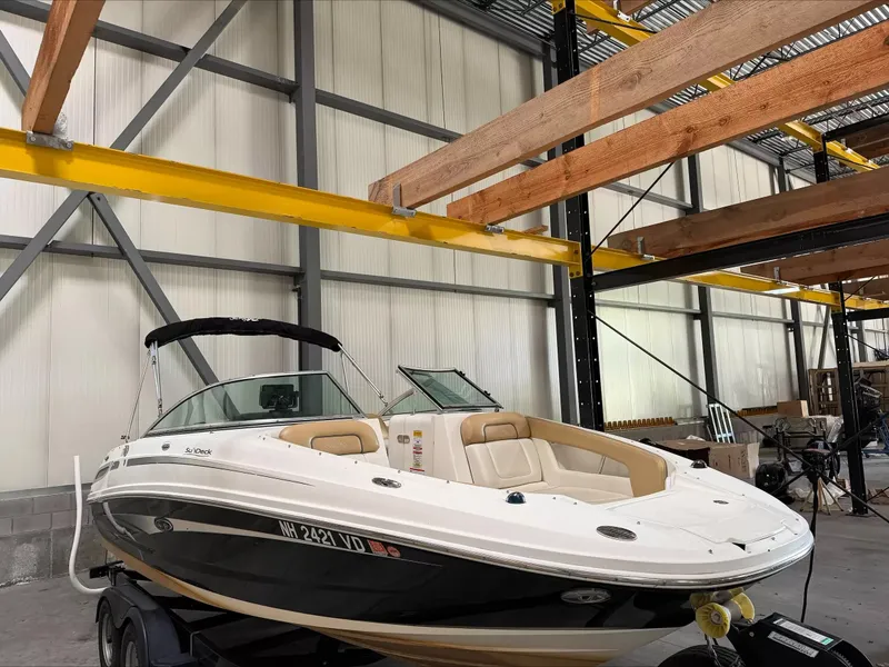 The Image of A 2011 Sea Ray 220 Sundeck boat is in a warehouse on a trailer. - 1