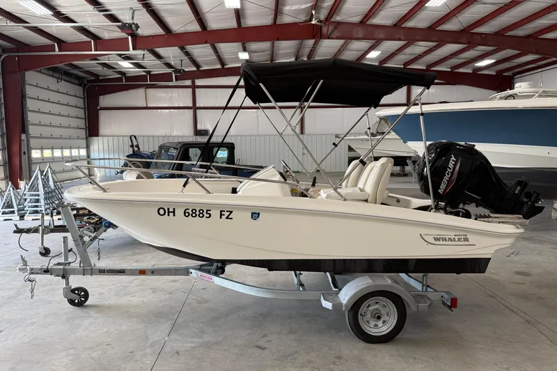 Slide: The Image of 2021 Boston Whaler 130 Super Sport boat with trailer in a spacious indoor storage facility. - 2