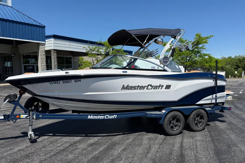 The Image of 2021 MasterCraft XT21 boat on trailer, parked outside a building under clear blue sky. - 1