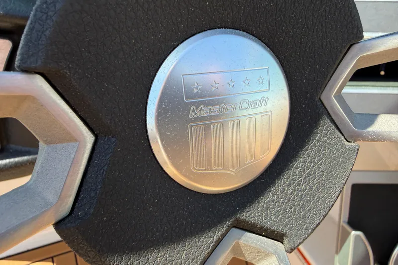 Slide: The Image of Close-up of 2021 MasterCraft XT21 steering wheel emblem, featuring a metallic finish. - 25