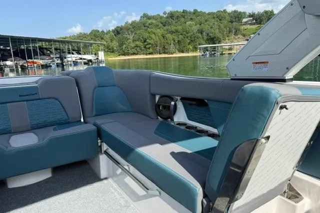 Slide: The Image of 2025 MasterCraft X24 boat interior with blue and gray seating, docked by a serene lake. - 10