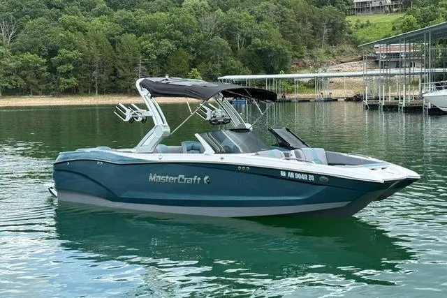 Slide: The Image of 2025 MasterCraft X24 boat on a serene lake with lush green surroundings. - 2