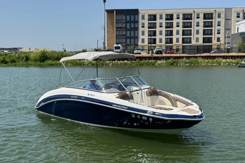 Slide: The Image of 2011 Yamaha Boats 242 Limited on calm water near modern buildings. - 5
