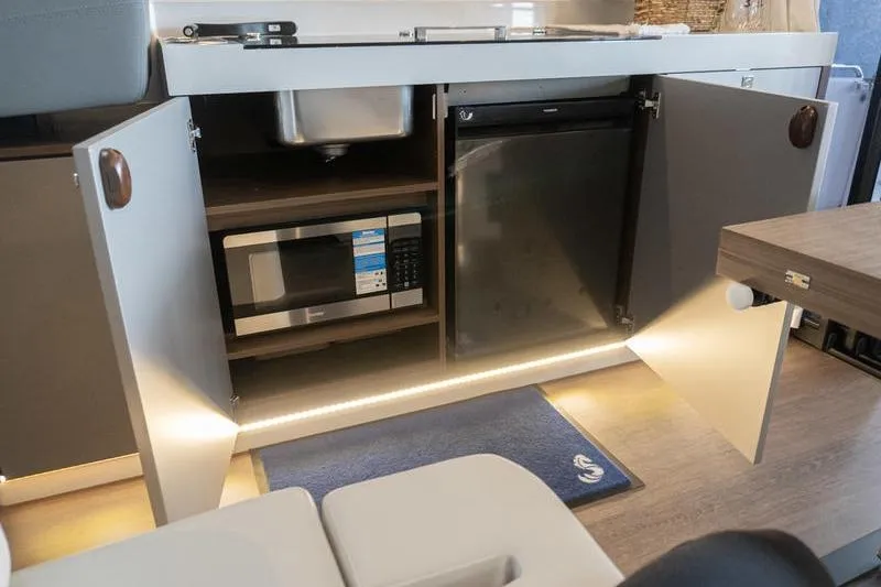 Slide: The Image of Interior view of 2026 Beneteau Antares 11 Coupe kitchen with open cabinets, microwave, and fridge. - 14