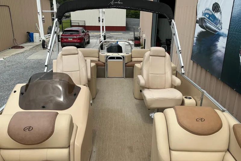 Slide: The Image of 2019 Avalon Catalina Quad Lounge boat interior with beige seating and helm, docked in a marina. - 2