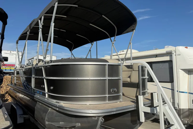 Slide: The Image of 2023 South Bay 224RS LE pontoon boat with canopy, parked near RVs under clear blue sky. - 4